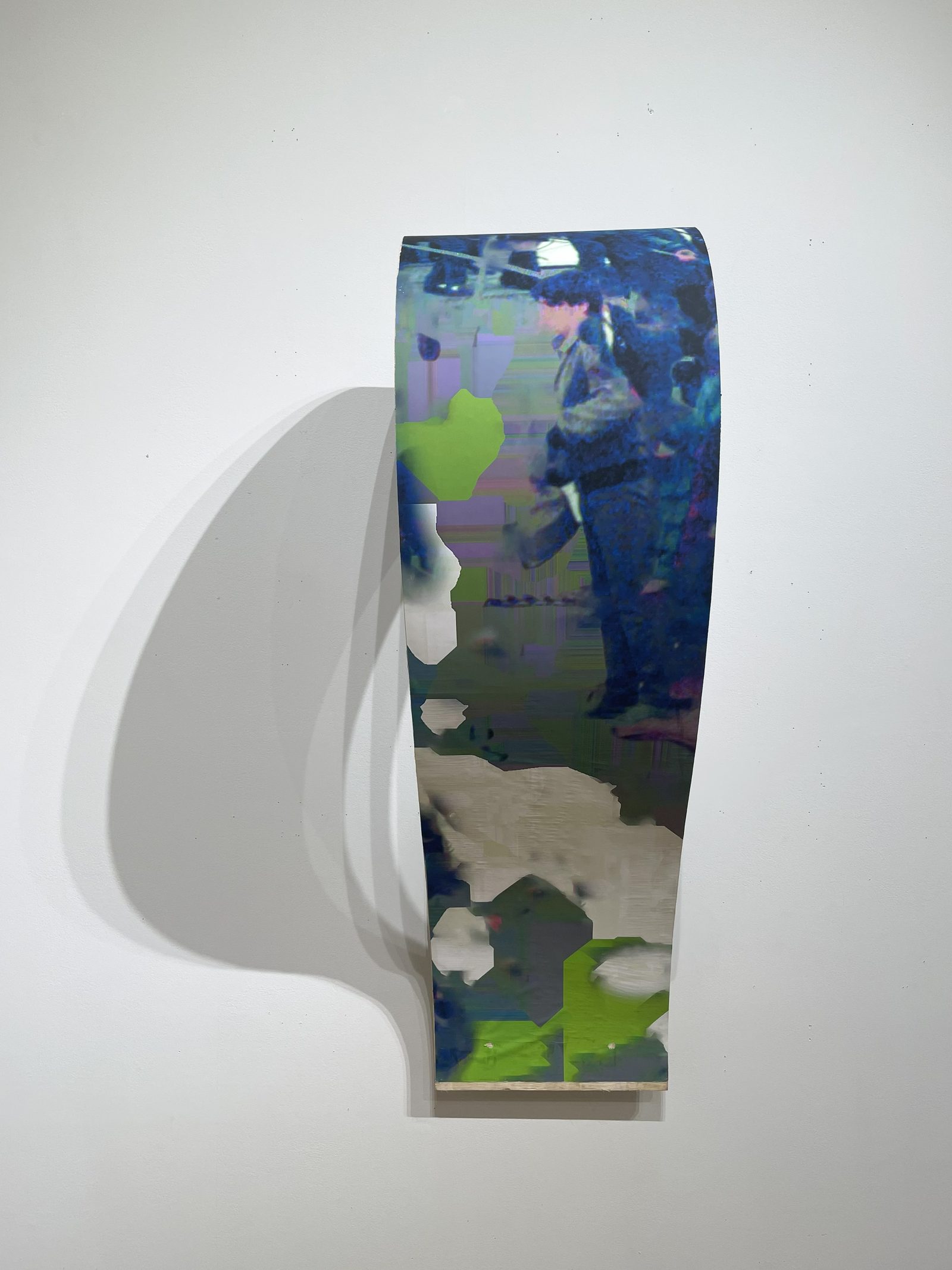 Curved plywood form on a white wall, wrapped in the print’s blue and lime-green image, casting a soft shadow.