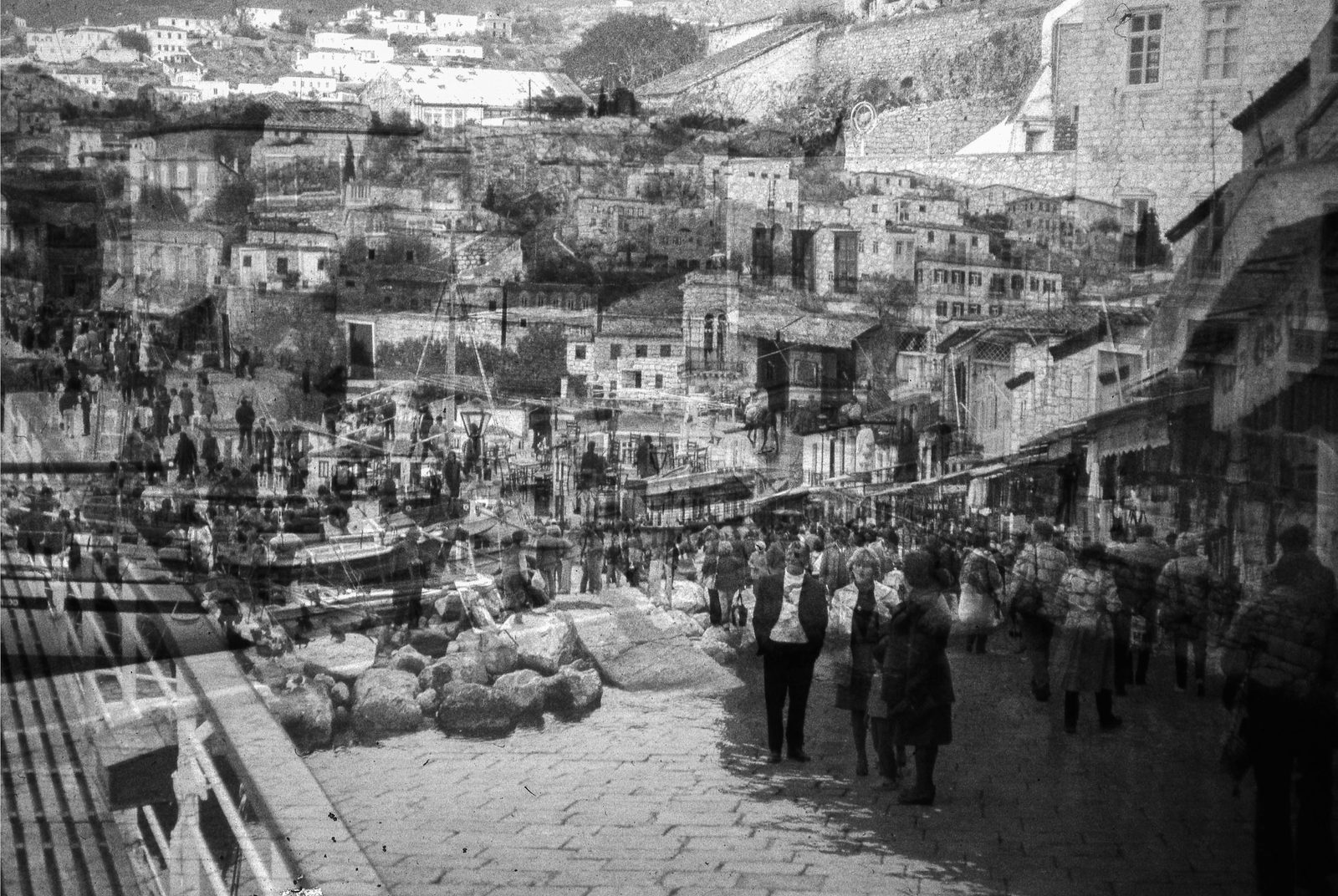 Black-and-white overlap of a crowded harborfront and a hillside town of stone houses.
