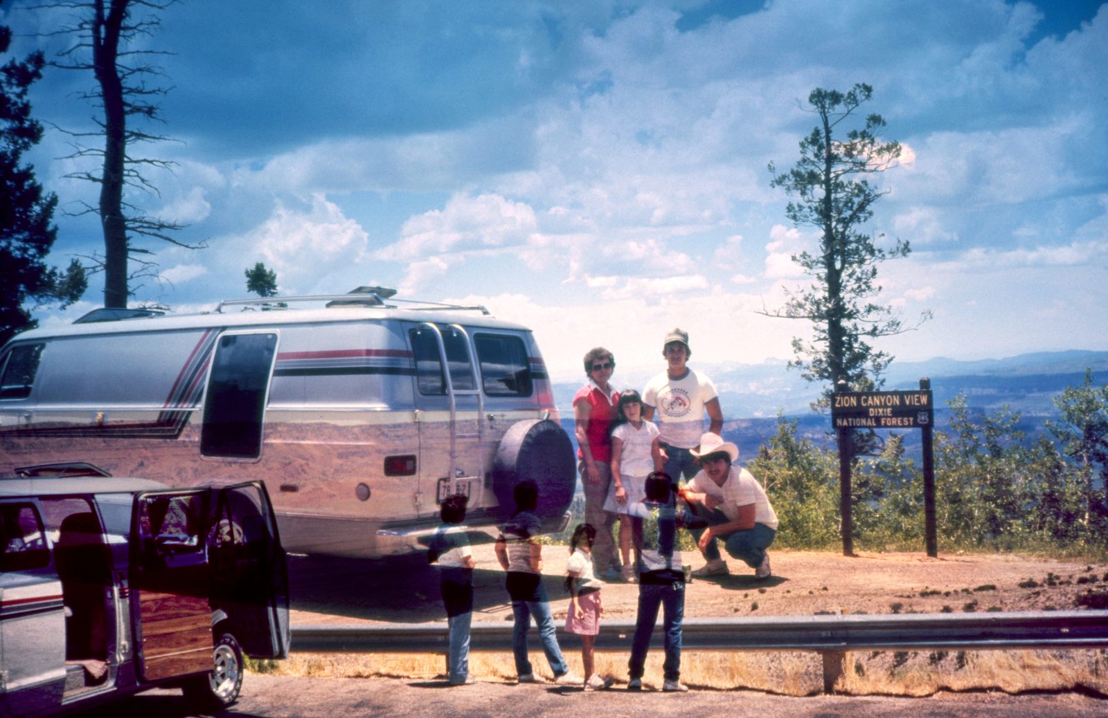 Family posed by a camper van at a Zion Canyon View sign, ghosted figures from a second slide in front.