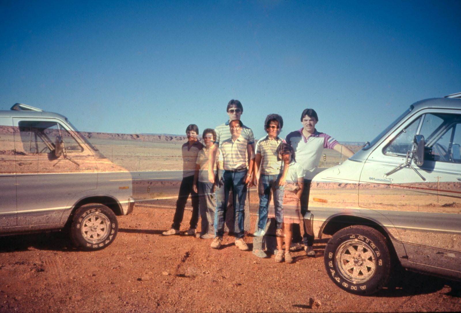 Family lined up between two vans in red desert, the halves meeting like a mirror.
