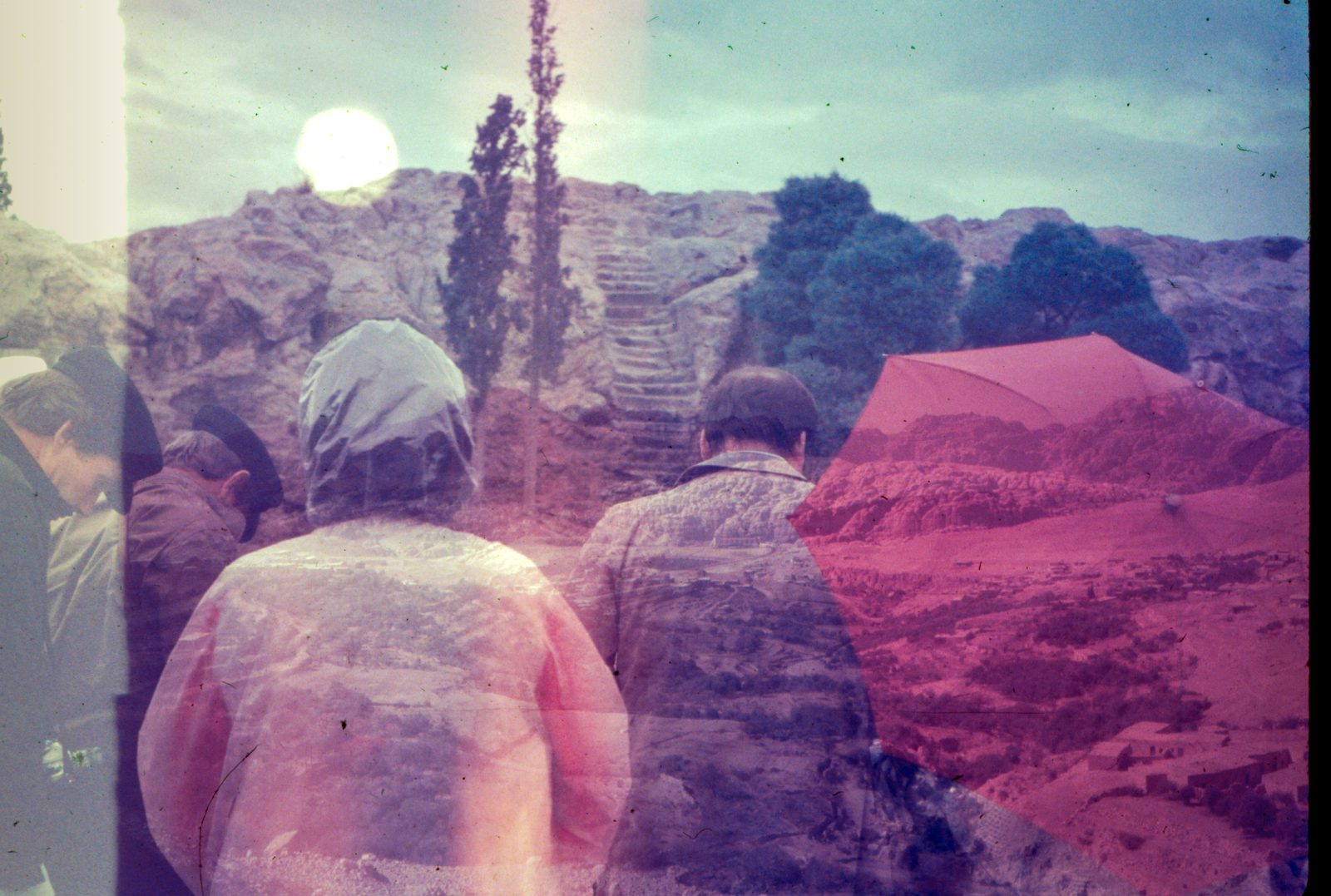 Figures in rain hoods seen from behind, facing stone steps and a pale sun, half the scene flooded in red.