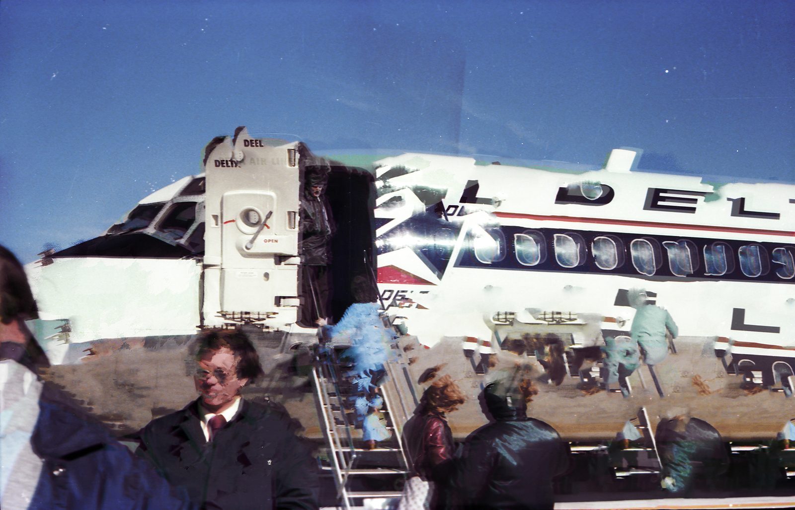 Passengers descending the stairs of a white airliner under a deep blue sky, figures ghosted and doubled.